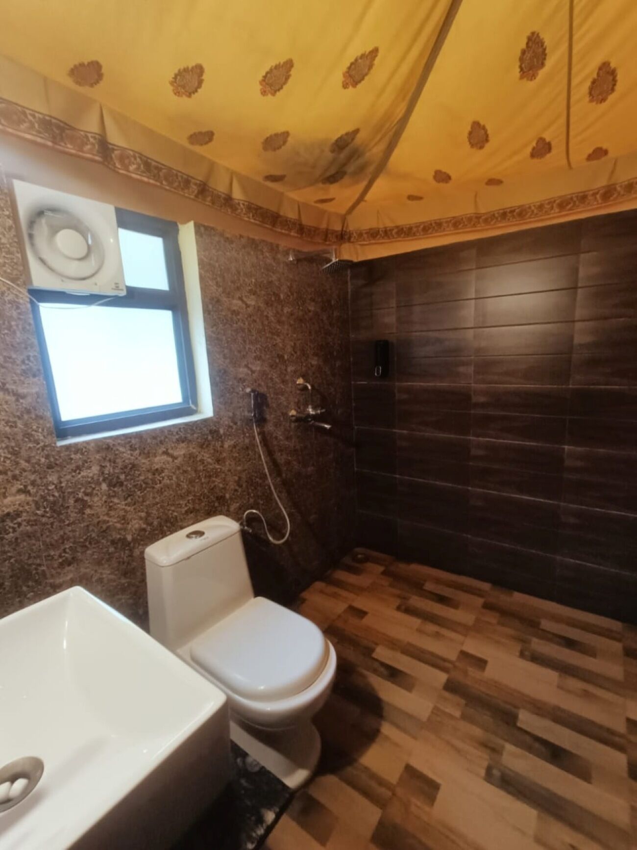 A bathroom with a toilet, sink, shower, and a window.