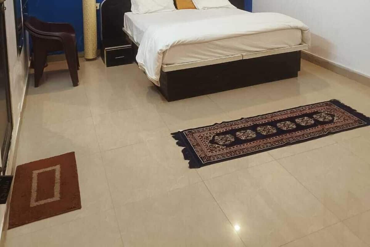 A bedroom with a bed, a ceiling fan, an air conditioning unit, a framed picture, and a small stool.