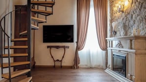 Eine Wendeltreppe führt zu einer zweiten Etage, ein Flachbildfernseher ist an der Wand montiert, ein Kamin mit Steinverkleidung sowie ein Fenster mit Vorhängen.