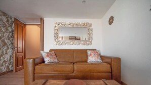Ein Wohnzimmer mit einem braunen Ledersofa, zwei gemusterten Zierkissen, einem Couchtisch aus Holz mit einer Schale, einem großen verzierten Spiegel und einer Holztür.