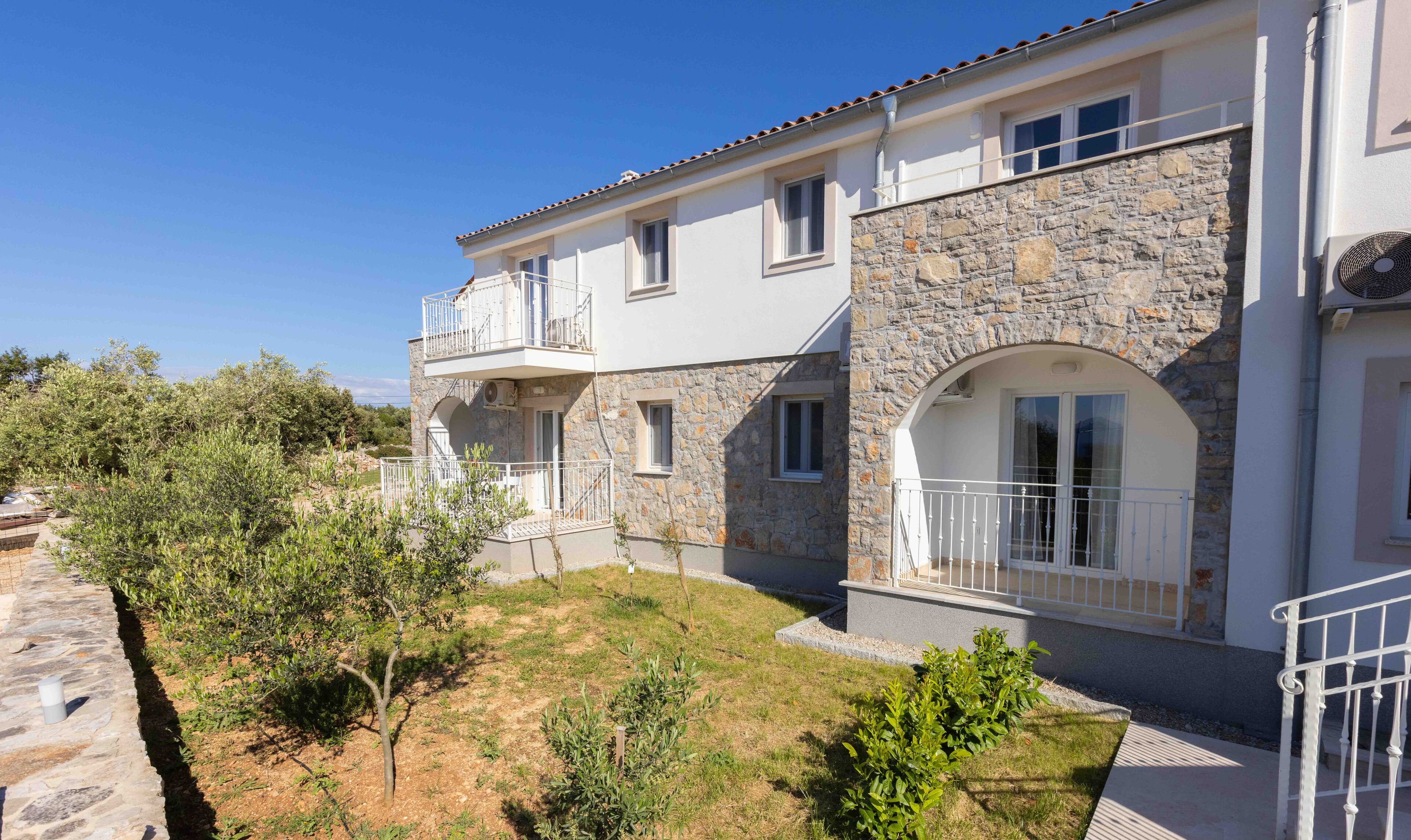 A two-story building with a stone facade, a balcony, and a small garden area.