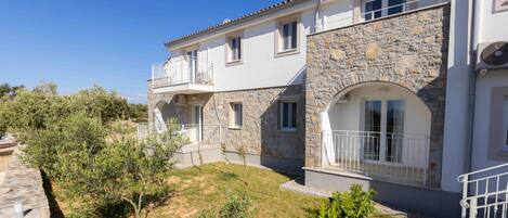A two-story building with a stone facade, a balcony, and a small garden area.