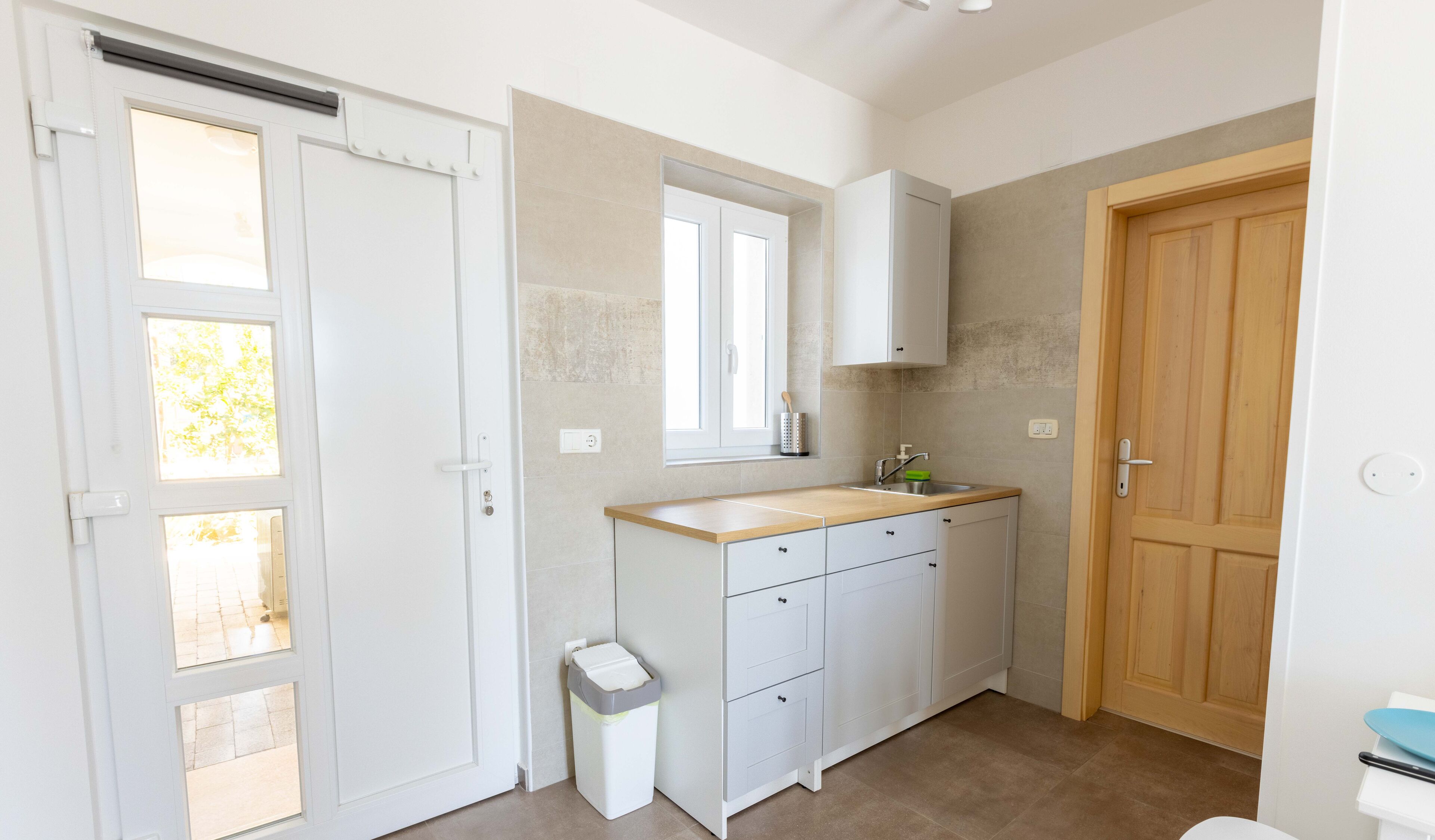 A compact kitchen with a wooden countertop, a window, and a wooden door.