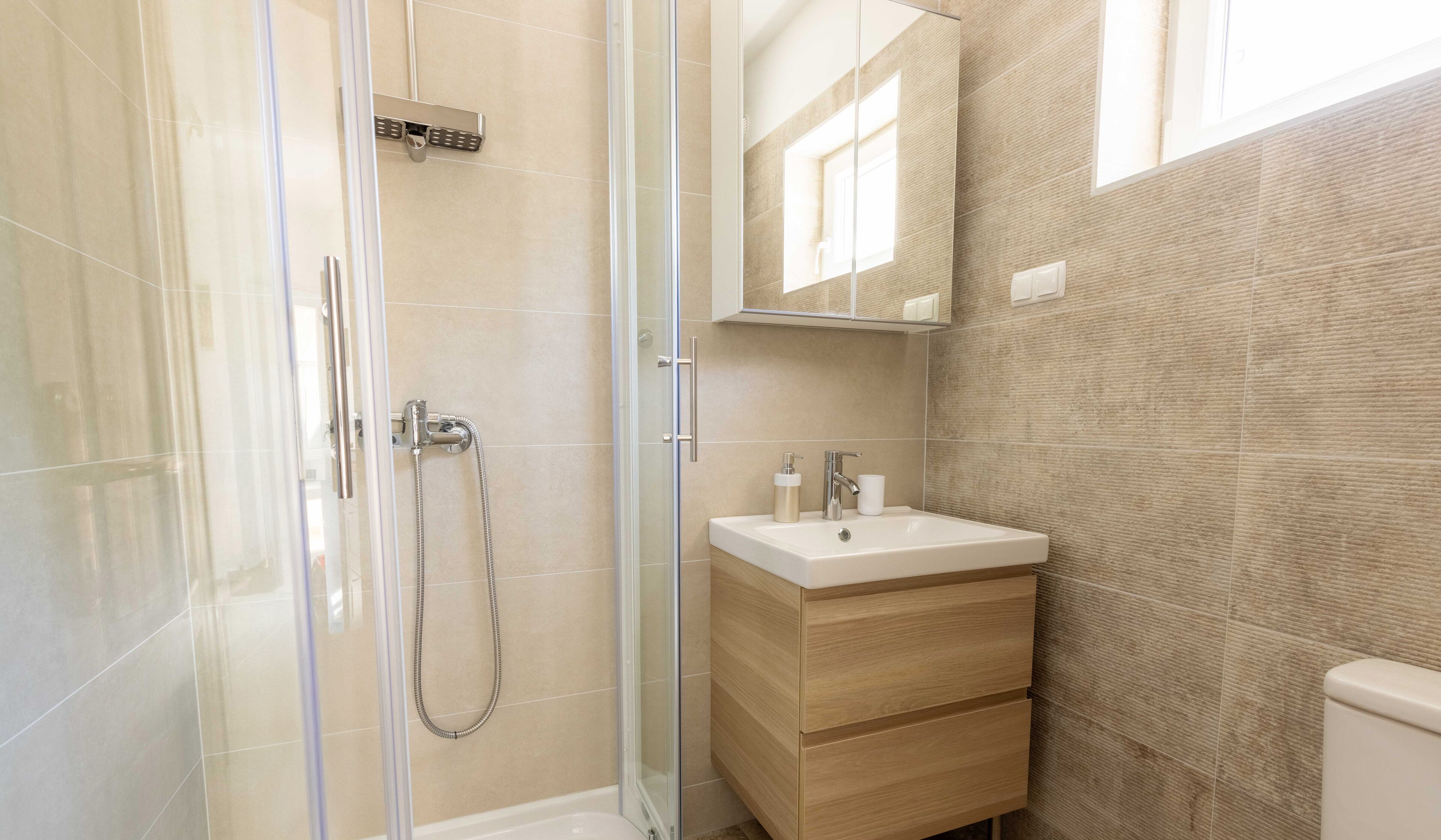 A modern bathroom with a glass shower enclosure, a wooden vanity with a sink, and a mirror above the vanity.