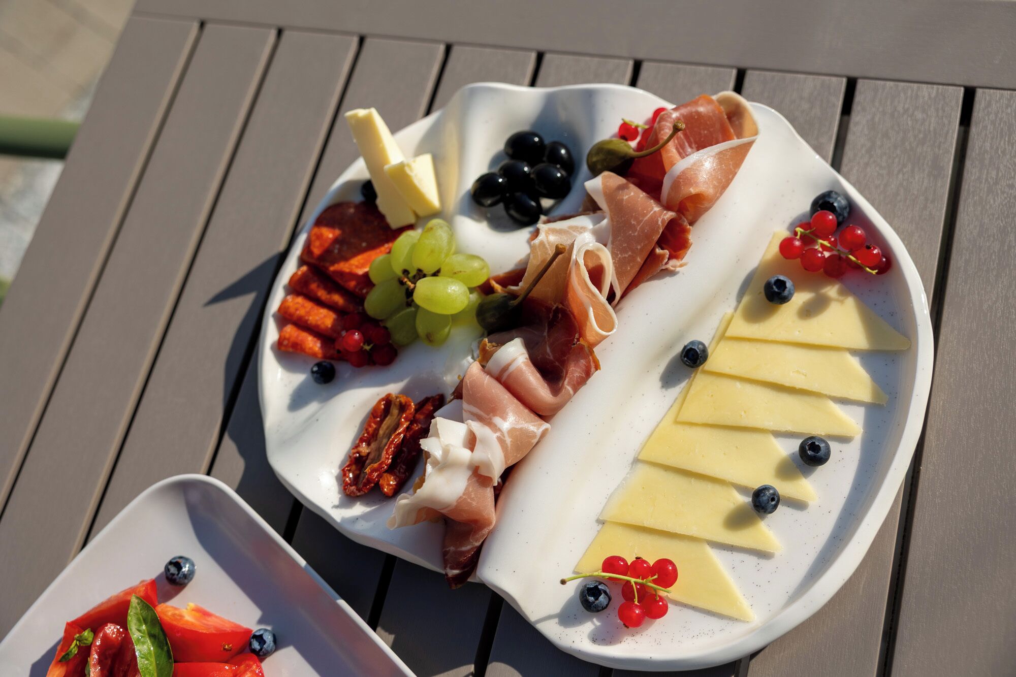 Una tabla de embutidos con diversos quesos, carnes y frutas sobre un plato blanco.
