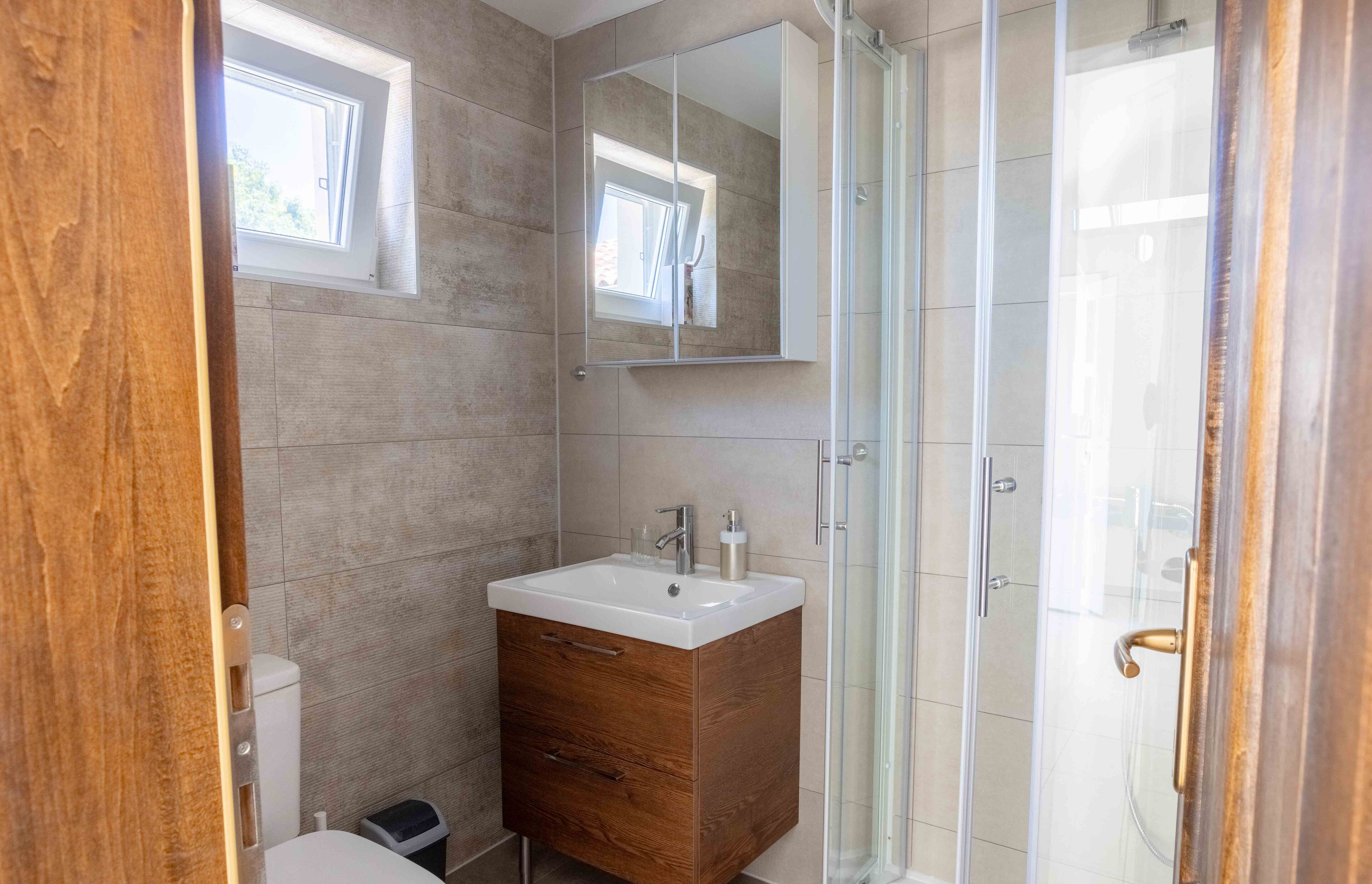 A modern bathroom with a wooden vanity, a large mirror, and a glass shower enclosure.