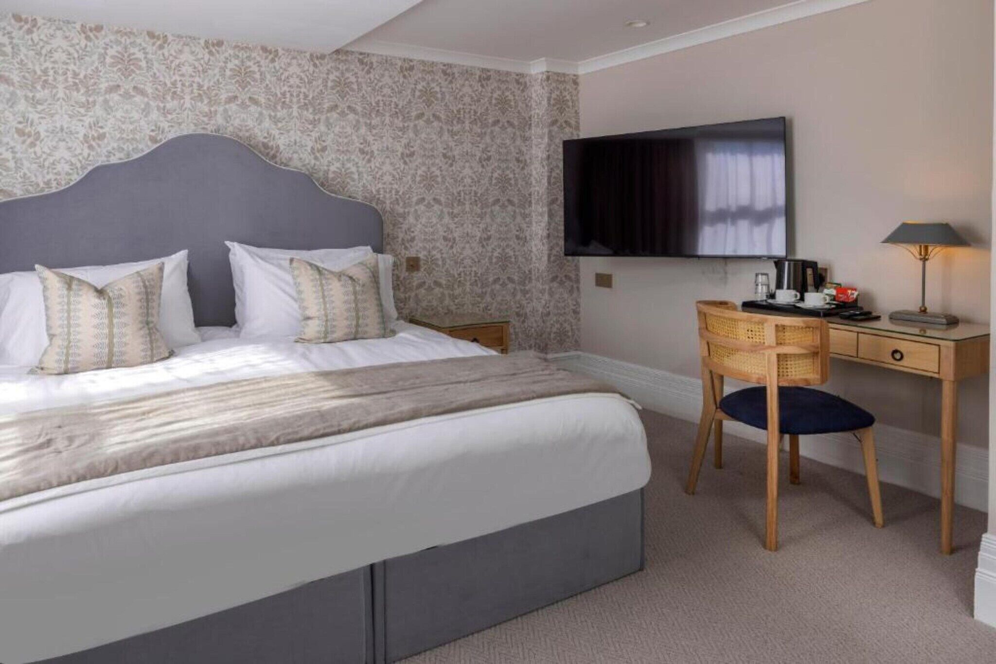 A bedroom with a bed, a desk, a chair, a television, and a lamp.