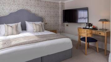 A bedroom with a bed, a desk, a chair, a television, and a lamp.