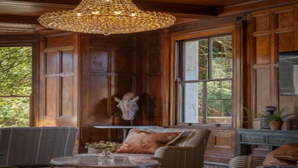 A room with wooden paneled walls, a large window, a chandelier, a sofa, and a table.