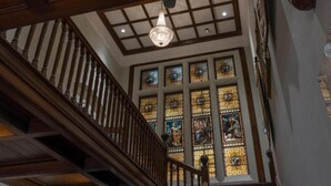 A grand staircase with a wooden handrail, a chandelier, and stained glass windows.