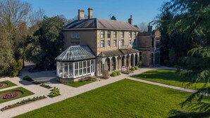 A large, historic building with a conservatory, formal garden, and a clear sky.