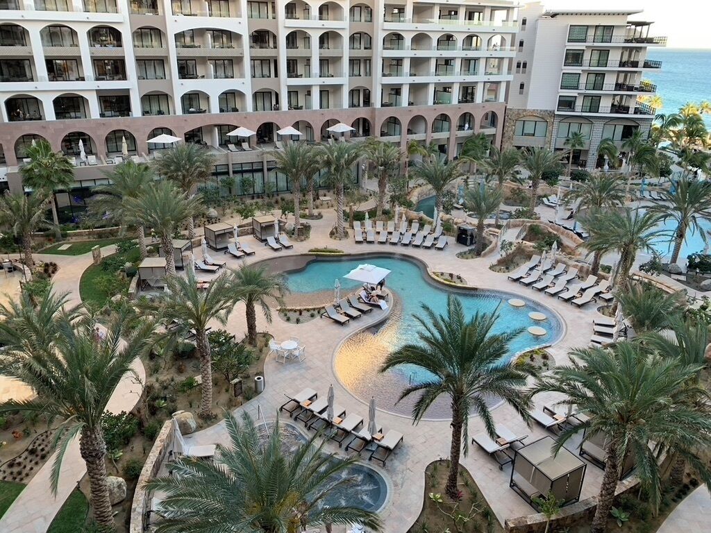 A resort with a central swimming pool surrounded by lounge areas and palm trees.