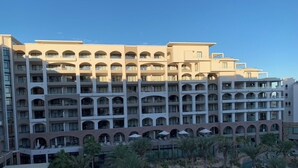Un hôtel à plusieurs étages doté d’une piscine, de palmiers et d’un espace extérieur aménagé avec des sièges.