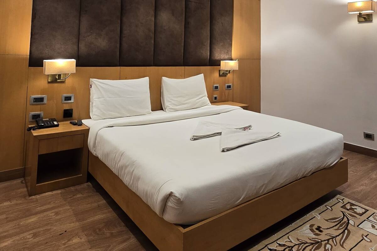 Una habitación de hotel moderna con una cama grande, cabecera de madera, mesitas de noche con lámparas y una alfombra estampada.