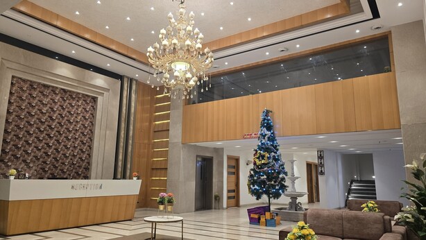 Un hall d  ’hôtel comprenant un comptoir d’accueil, un lustre, un sapin de Noël et un espace salon.