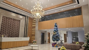 A hotel lobby with a reception desk, a chandelier, a Christmas tree, and a seating area.