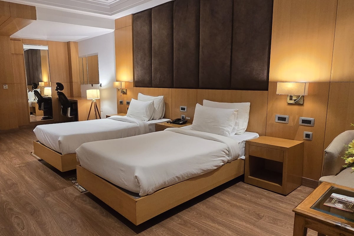 Habitación de hotel con dos camas, suelo de madera, un espejo grande y una pared oscura de acento.