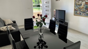 A modern living room with a glass-top coffee table, black chairs, a sofa with polka dot cushions, a flat-screen TV, a painting on the wall, and a door leading to a garden. - Apartment Paulina - 3-bedroom apartment in charming Trogir with WiFi, AC (Trogir)
