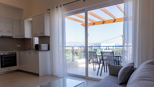 A modern kitchen with white cabinets and a microwave, a glass coffee table, and a sofa with cushions. - Phaedrus Living: Seaside Thalassa Cretan 201 (Platanias)