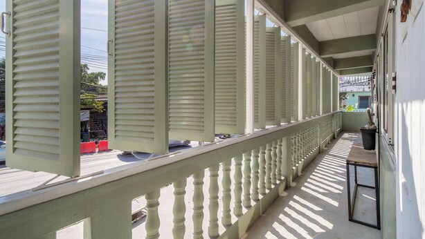 A covered balcony with a railing, a table, and a potted plant.
