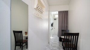 A hallway with a white wall, a wooden chair, a small table with a vase, and a coat rack.