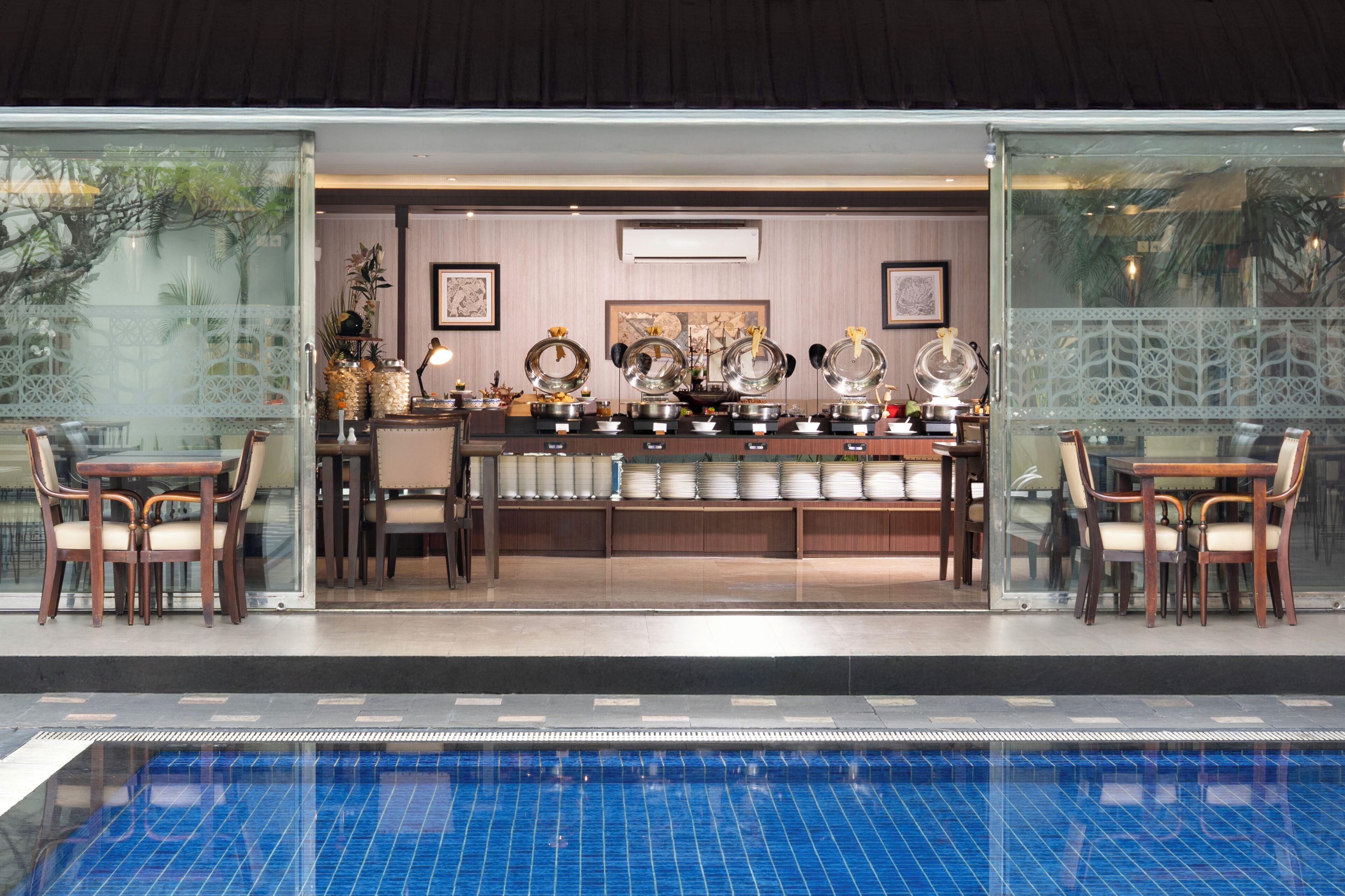 A poolside dining area with a glass partition, a pool, and a buffet setup.