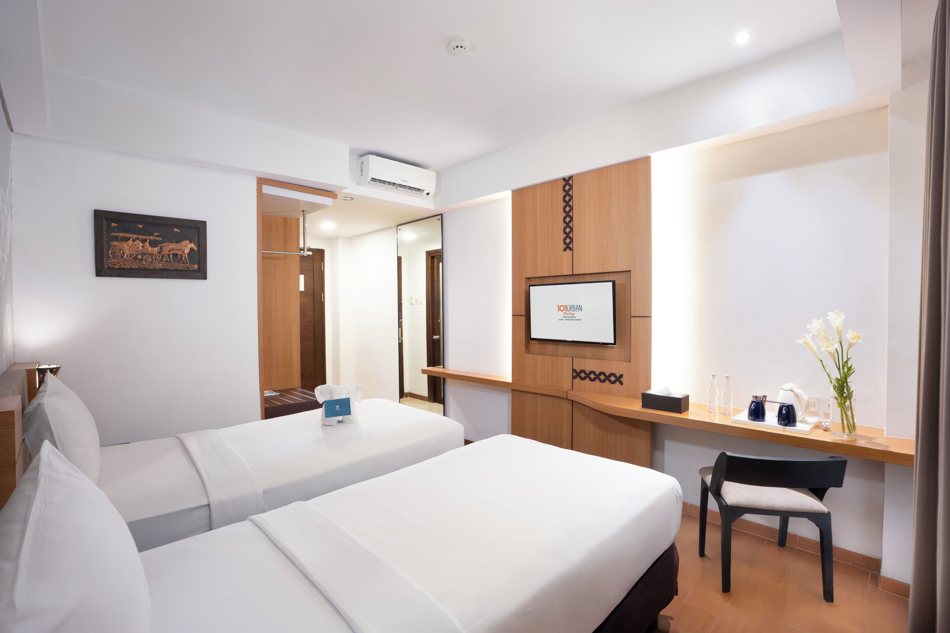 A hotel room with two beds, a desk, a chair, a TV, and a framed picture on the wall.