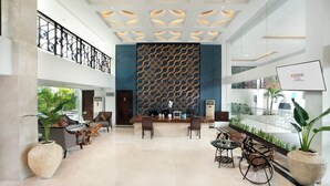 Een ruime lobby met een receptiebalie, zithoek en decoratieve wand.