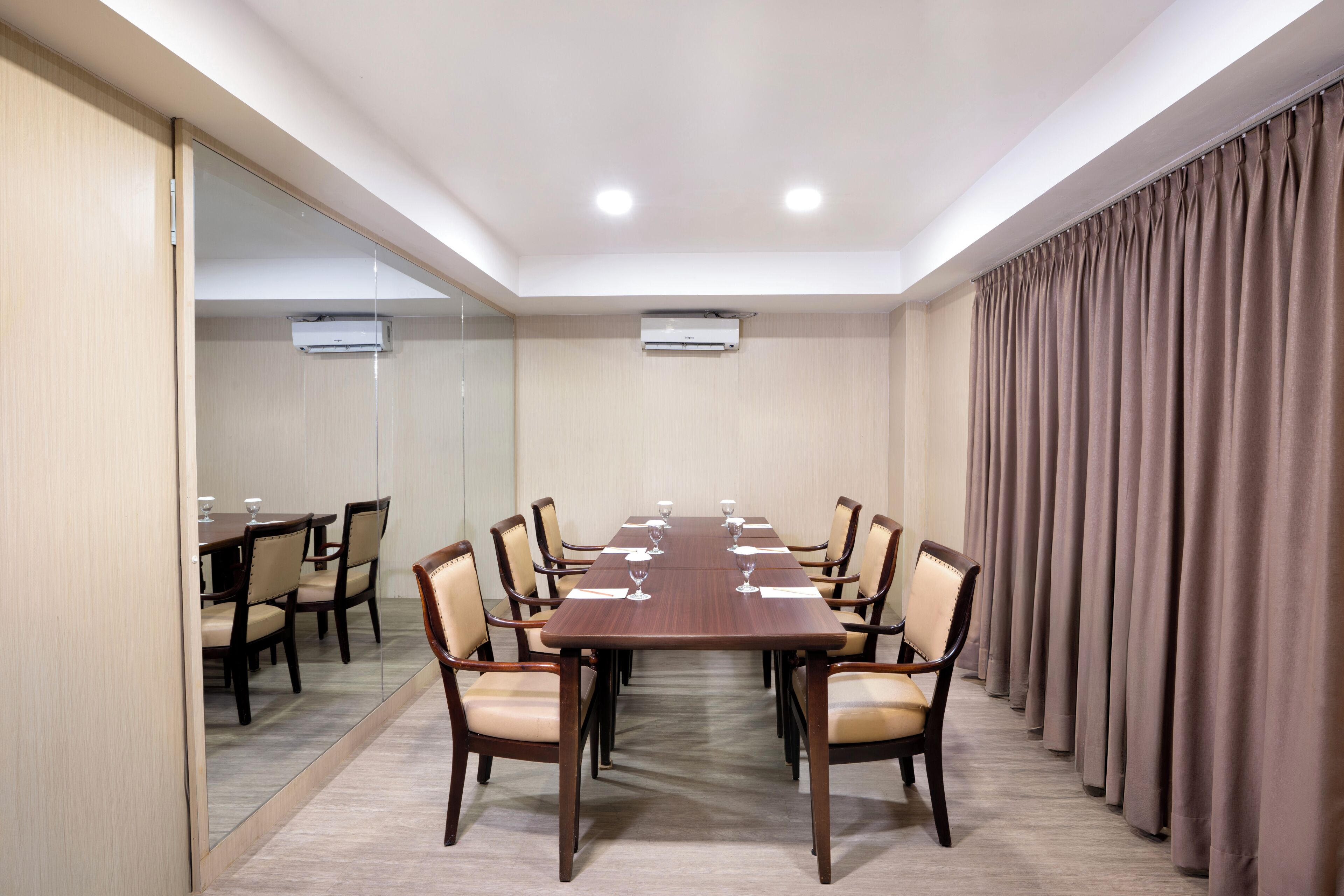 Uma sala de conferências com uma mesa comprida, cadeiras e um espelho em uma das paredes.