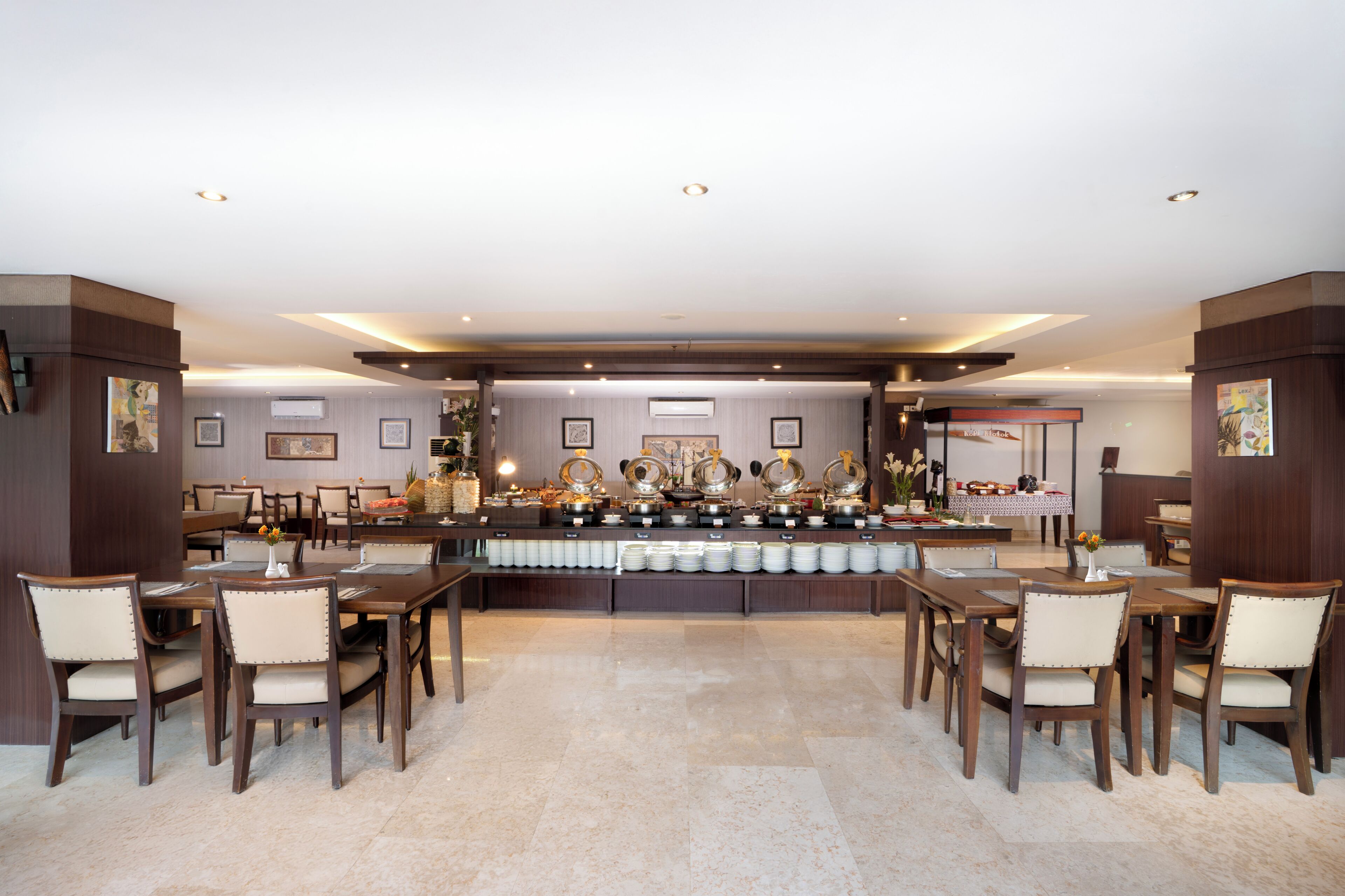 Un grand espace dédié à la salle à manger, avec de nombreuses tables et chaises, un buffet proposant divers plats et des œuvres d’art encadrées accrochées aux murs.