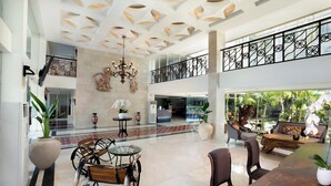 Een ruime lobby met een hoge plafond, een weelderige kroonluchter, een zithoek met banken en stoelen, en een uitzicht op het exterieur door grote ramen.