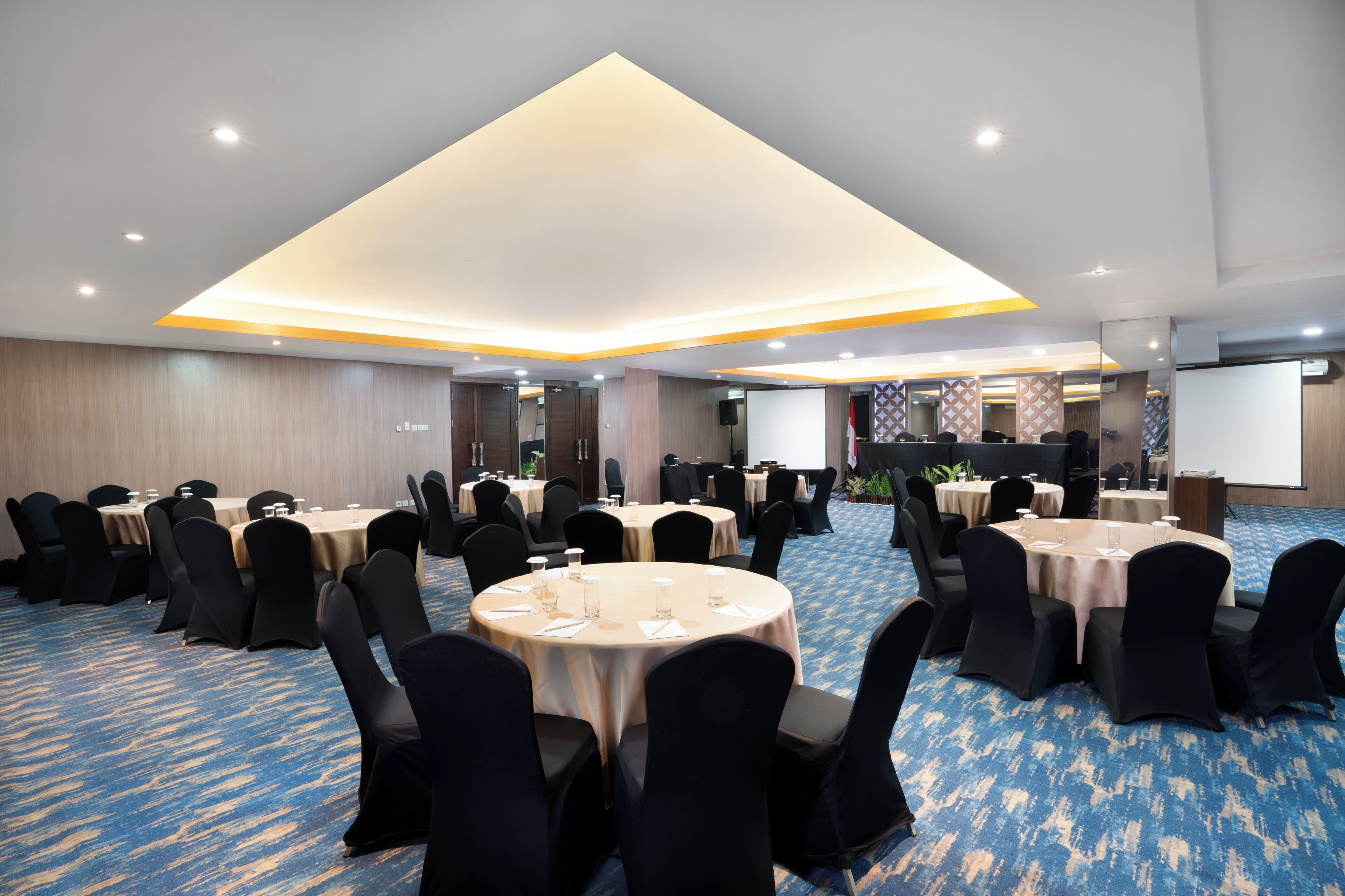 Une salle de conférence avec des tables rondes, des chaises noires et un sol recouvert d’une moquette bleue.