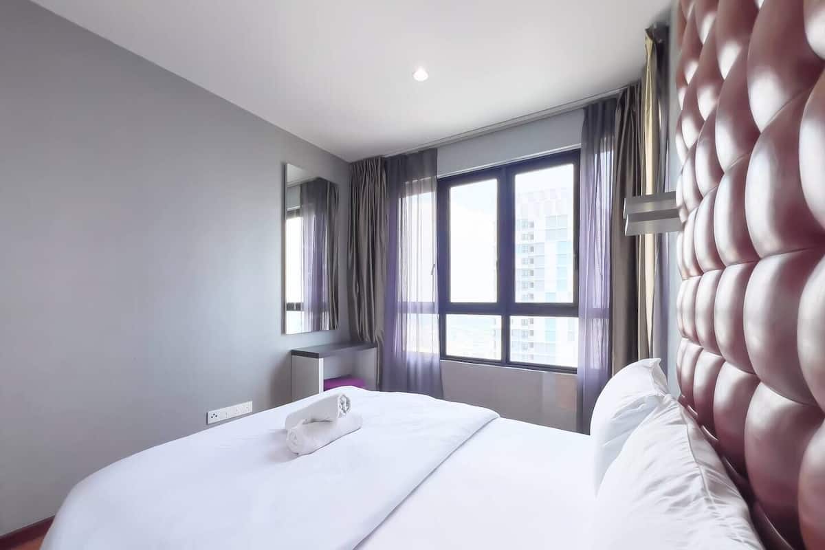 Une chambre d’hôtel moderne avec un grand lit, un miroir, une fenêtre avec des rideaux et une vue sur les bâtiments environnants.