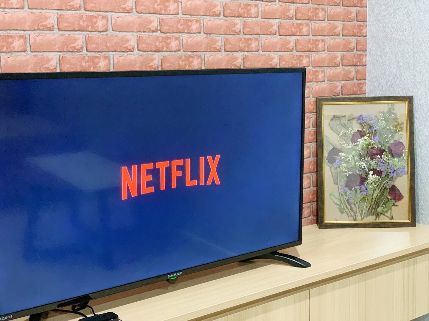 Ein Fernseher mit Netflix-Logo auf blauem Bildschirm, auf einer Holzfläche vor einer Backsteinwand.