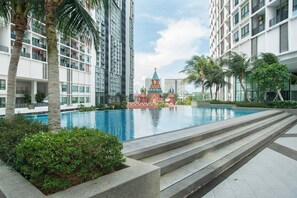 Un moderno edificio residencial con piscina, palmeras y una pequeña estructura decorativa.