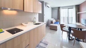 A modern kitchen with a sink, countertop, and wooden cabinets. There is a dining area with a table and chairs, and a sofa. - I City Luxury Condo Shah Alam Smarthome (Shah Alam)