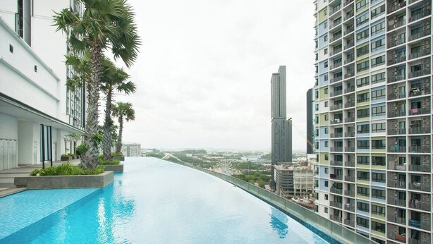 Uma piscina infinita no terraço com vista para a cidade, cercada por edifícios modernos e palmeiras.