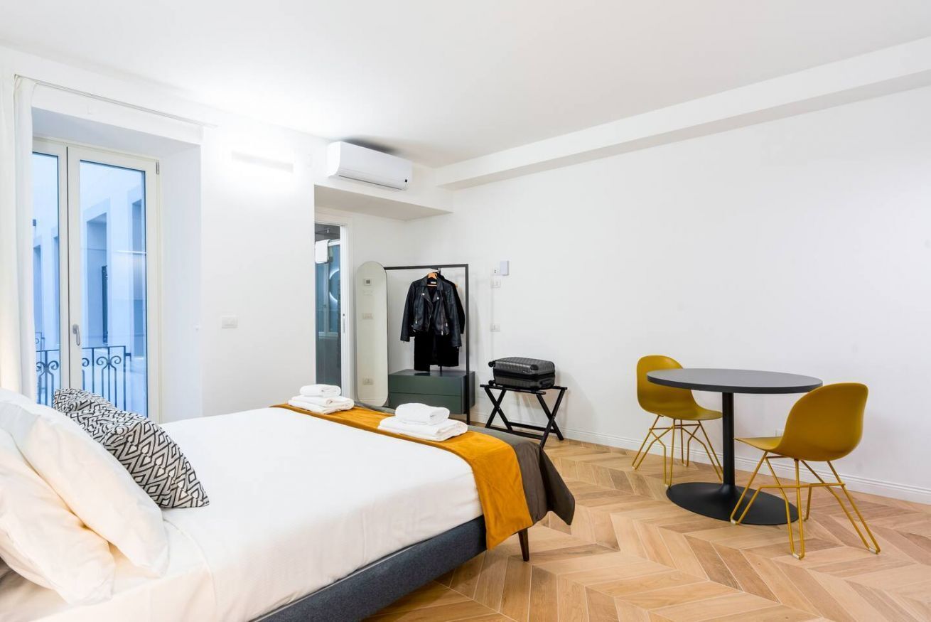 A hotel room with a bed, a table with chairs, a mirror, and a wardrobe.