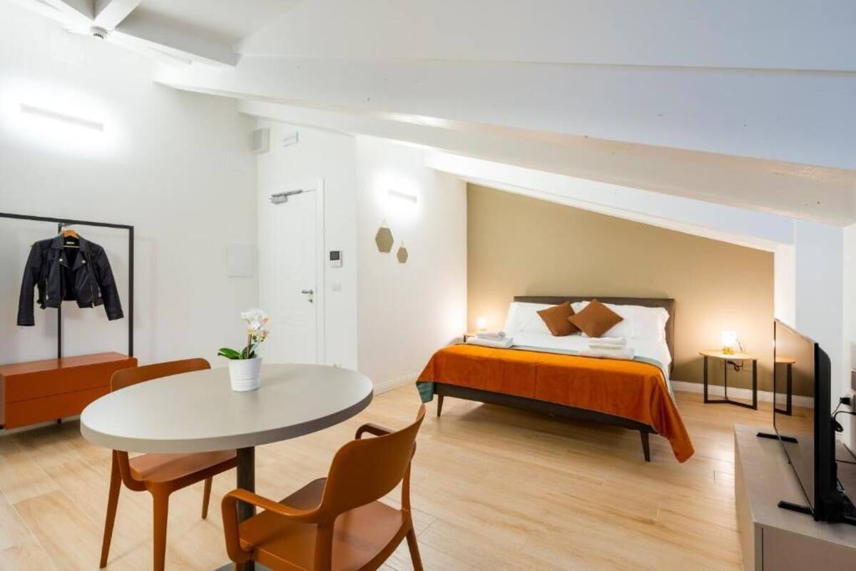 A hotel room with a bed, a round dining table with chairs, a TV, and a coat rack with jackets.