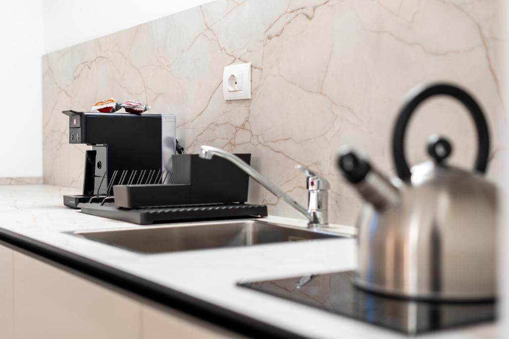 A modern kitchen with a built-in coffee maker, a kettle, and a marble backsplash.