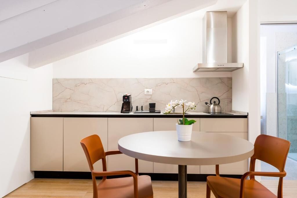 A modern kitchen with a marble backsplash, a stainless steel range hood, and a round table with two chairs.