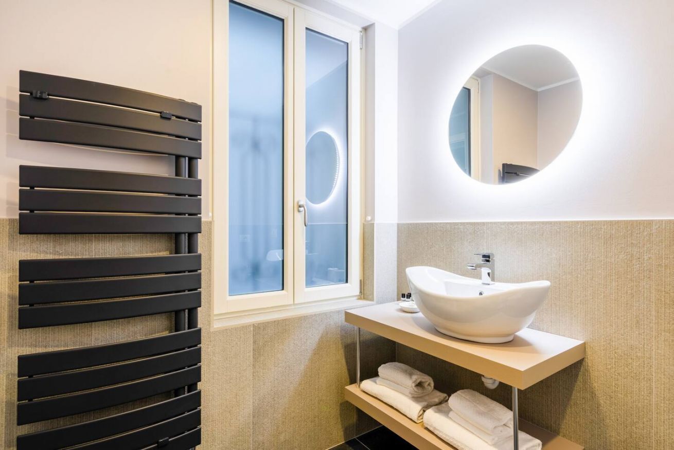 A modern bathroom with a black slatted wall, a white sink, and a round mirror.