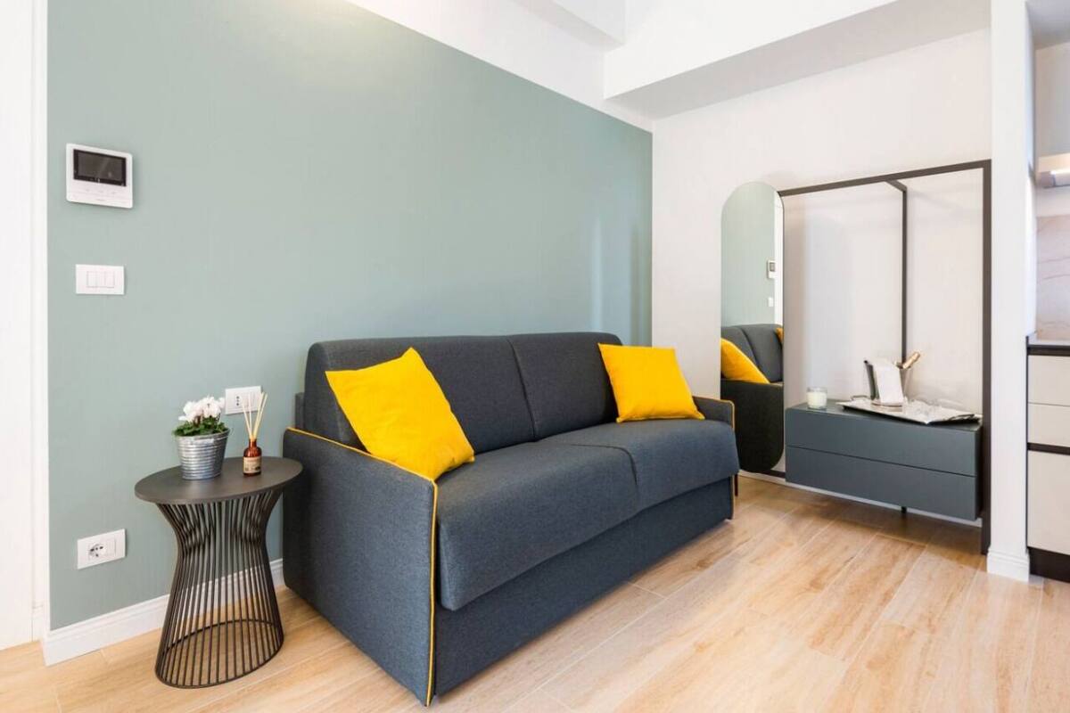 A modern living room with a grey sofa, yellow cushions, a small round side table, and a mirror on the wall.