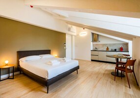 Una camera da letto con un letto grande, un comodino con una lampada e vista su un angolo cucina con un tavolo e sedie.