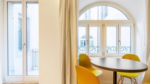 A room with a round table and yellow chairs, a large arched window, and a sliding glass door leading to an outdoor balcony. - JOIVY Premium Apartments Trieste Mazzini (Trieste)
