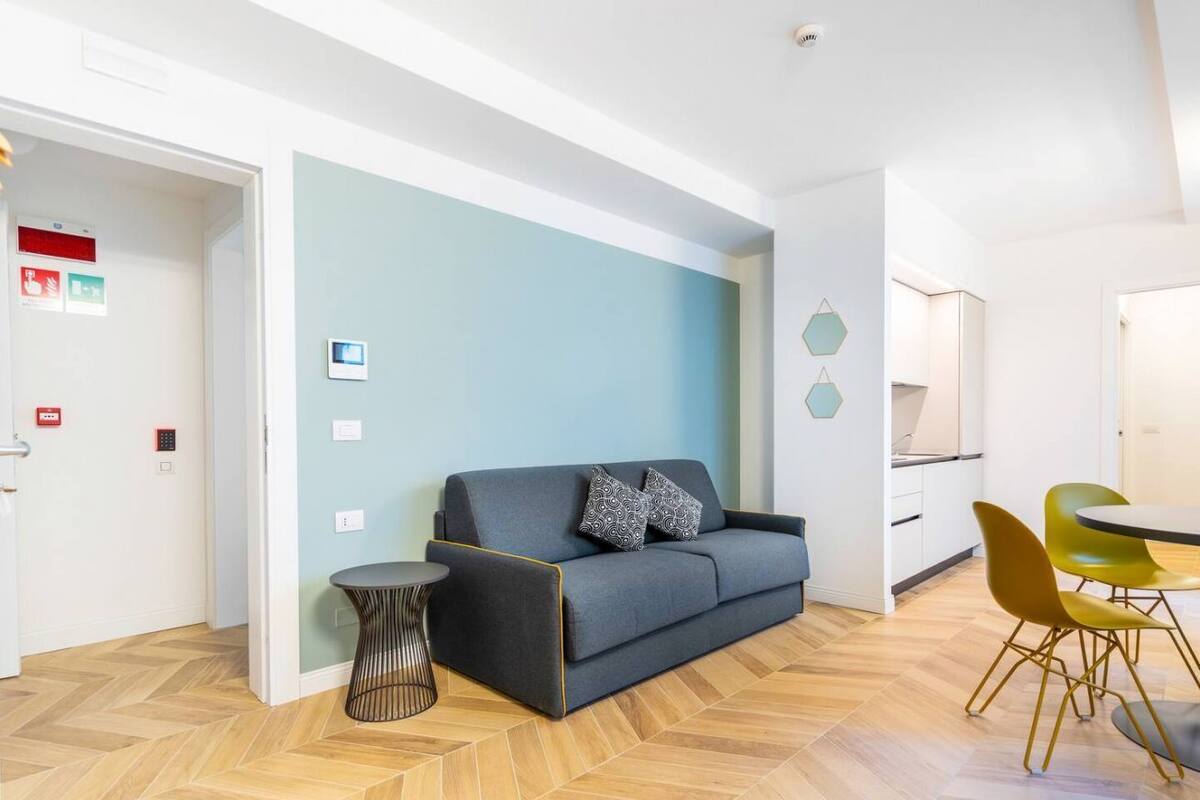 A modern living room with a sofa, a small side table, and a dining area with chairs.