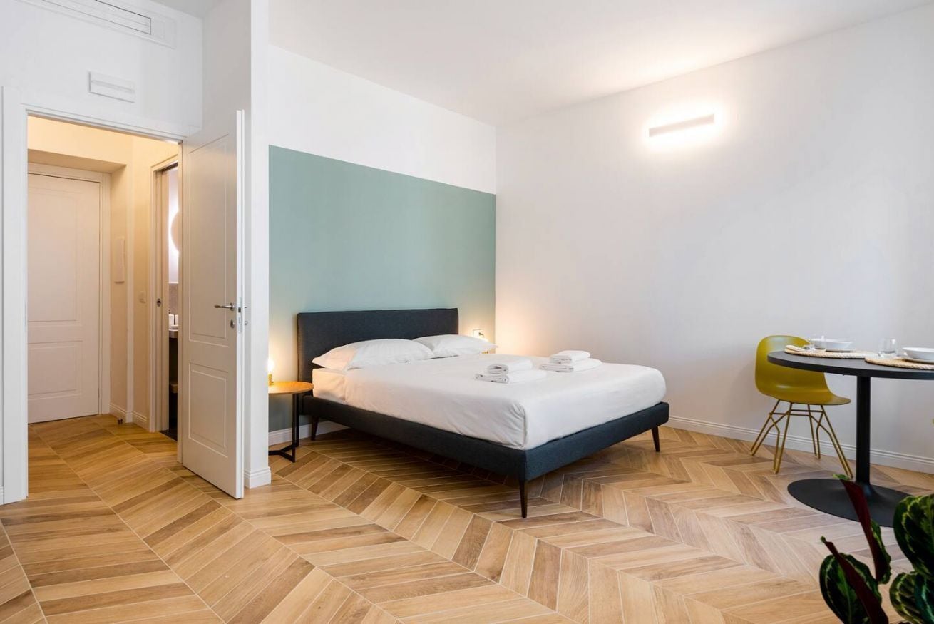 A bedroom with a bed, a bedside table, a chair, and a table with a lamp.