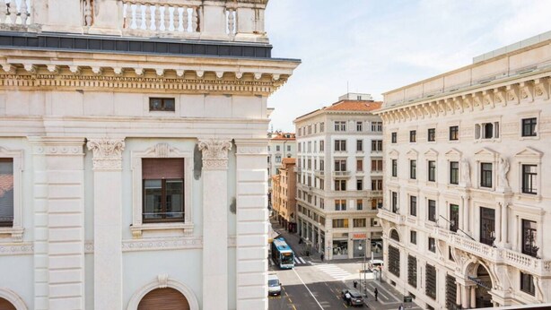 A street view with classical architecture, including a building with a balcony and a row of windows. - JOIVY Premium Apartments Trieste Mazzini (Trieste)