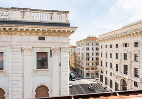 Una vista di una strada con architettura classica, che include un edificio con un balcone e una fila di finestre.