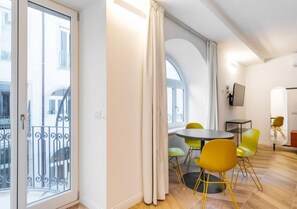 A modern apartment with a balcony, a dining area with yellow chairs, and a TV mounted on the wall. - JOIVY Premium Apartments Trieste Mazzini (Trieste)